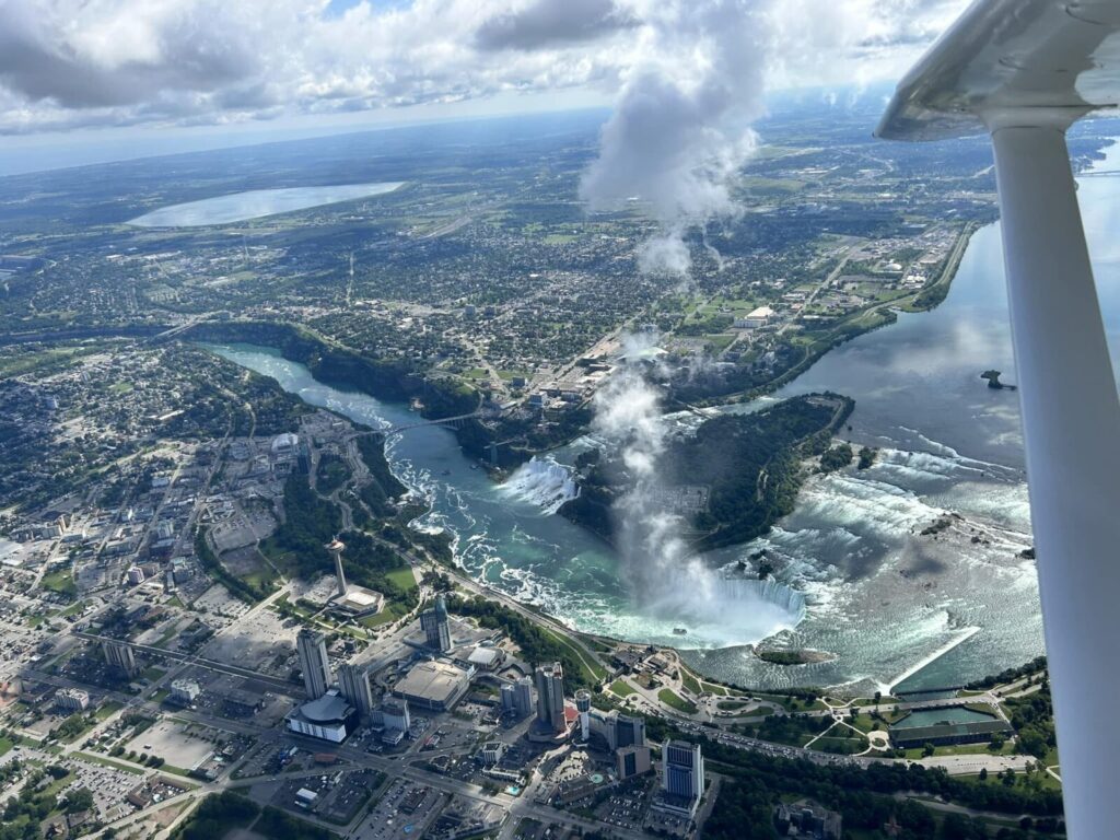 Aerial view of Niagara Falls and surrounding cityscape, with mist rising from the waterfalls under partly cloudy skies.
